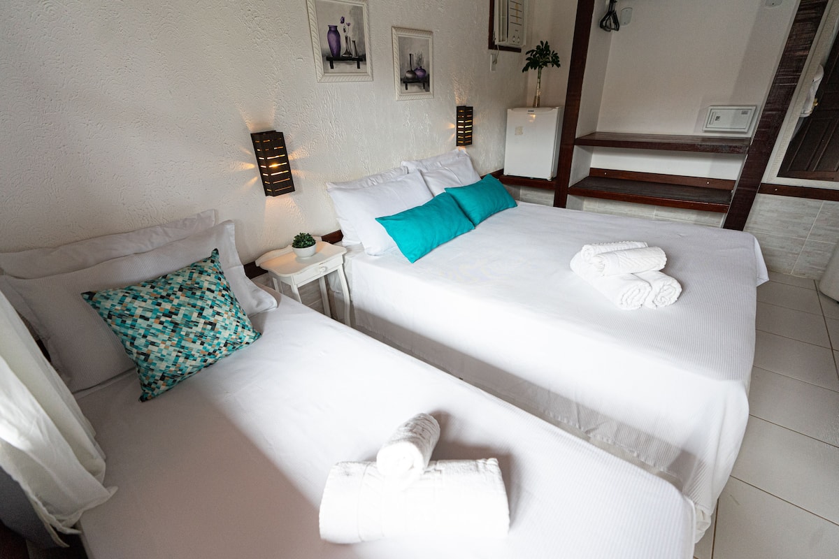 A hotel room with two beds, white bedding, teal pillows, and a small table with a plant.