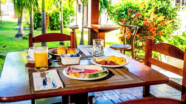 A breakfast table set outdoors with plates of food, a glass of orange juice, and a cup of coffee. - Pousada Maria Maria Buzios (Búzios)