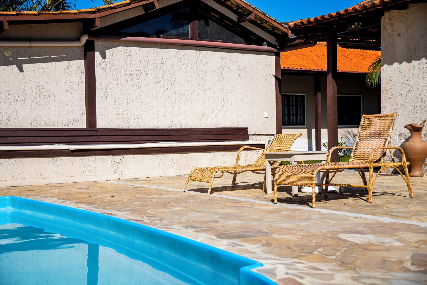 A poolside area with wicker lounge chairs and a stone-tiled floor.