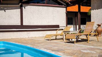 A poolside area with wicker lounge chairs and a stone-tiled floor.