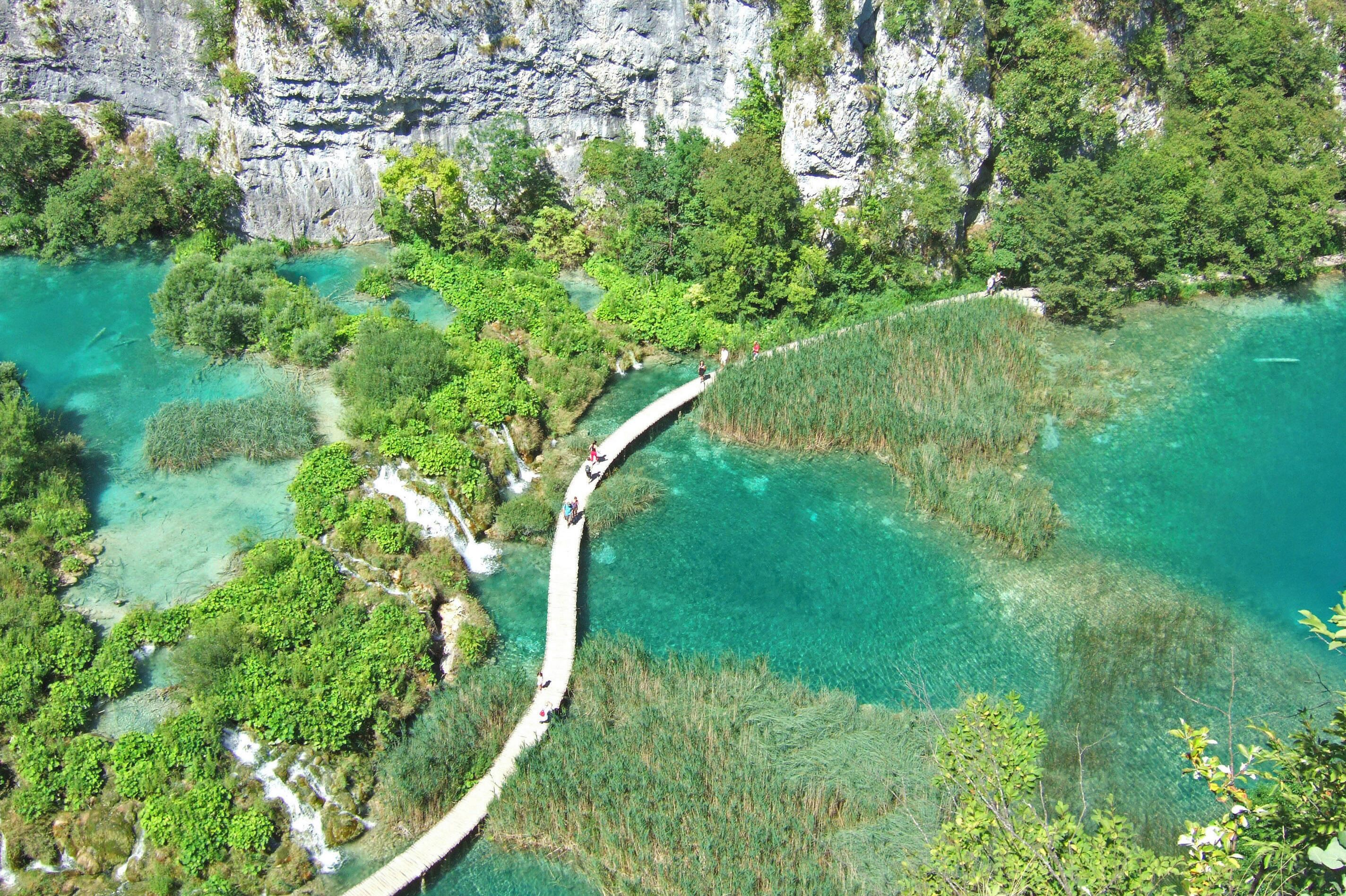 Ein klarer Luftbildblick auf eine Küstenlandschaft mit einer weißen Brücke, die zwei Landmassen verbindet, umgeben von üppigem Grün und klarem türkisblauem Wasser.