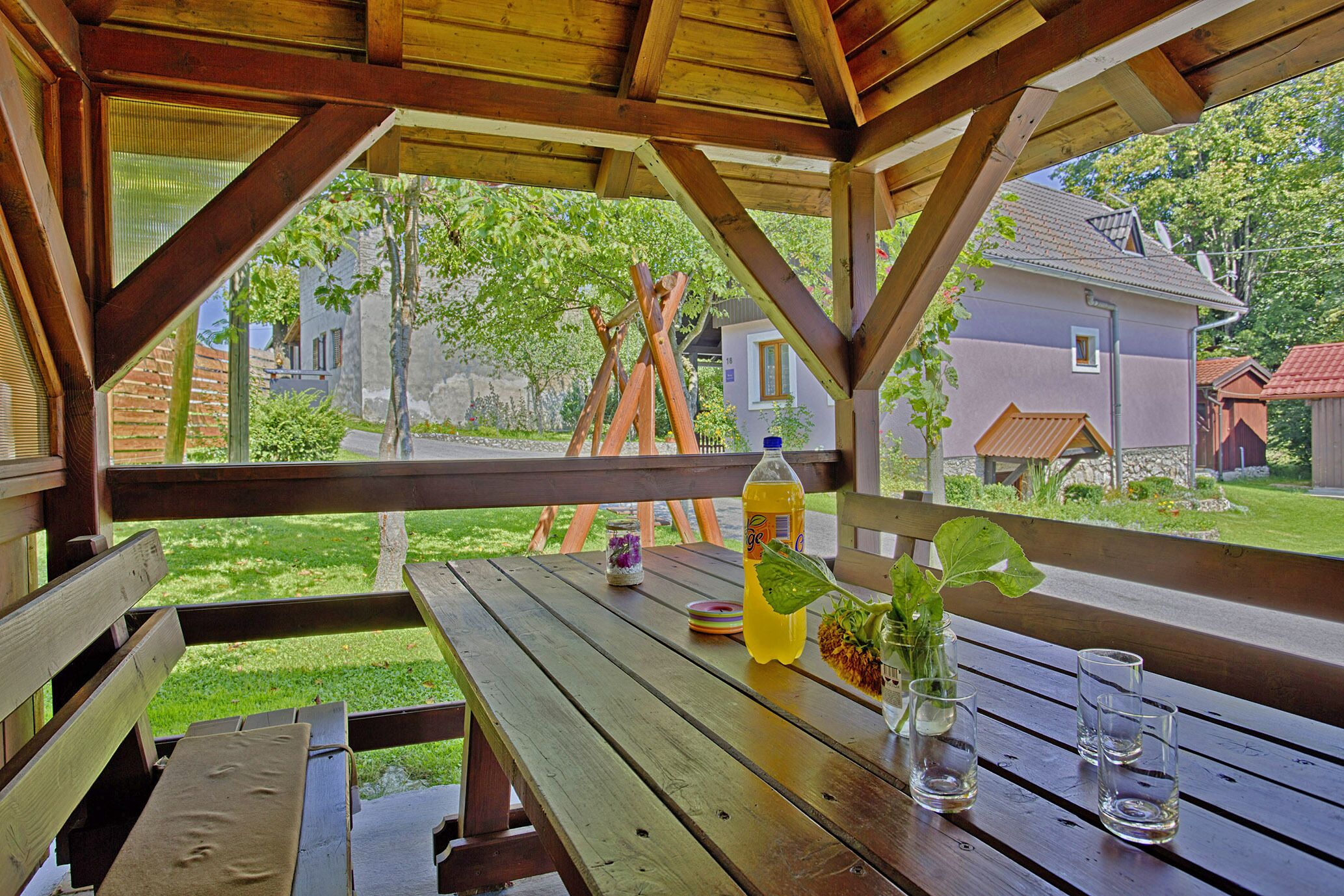 An outdoor wooden pavilion with picnic tables, a bottle of lemonade, and a glass of water.