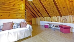 A cozy attic room with a wooden ceiling, a white sofa with patterned cushions, a small table, and a pink ottoman. - Andrea in Sertić Poljana  - Haus für 6 Personen (Plitvička jezera)