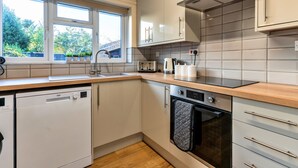 Een compacte keuken met witte kasten, een vaatwasser, een oven en een raam dat voor natuurlijk licht zorgt.