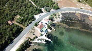 An aerial view of a coastal road with a bridge, a small settlement with houses, and a clear view of the sea.