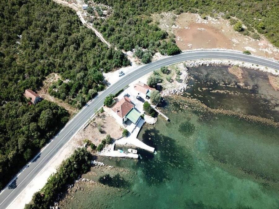 Vista aérea de una carretera costera con un puente, un pequeño poblado con casas, y una vista despejada del mar.