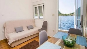 A compact living space with a sofa, a dining table with a glass bowl, and a view of the water. - Apartment Pascal (Janjina)