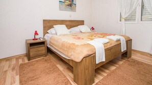 A neatly arranged bedroom with a wooden bed, a nightstand, a red lamp, and a painting on the wall. - Apartment Pascal (Janjina)