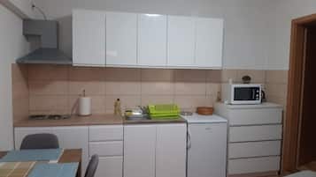 A compact kitchen with white cabinets, a microwave, a sink, and a small refrigerator.