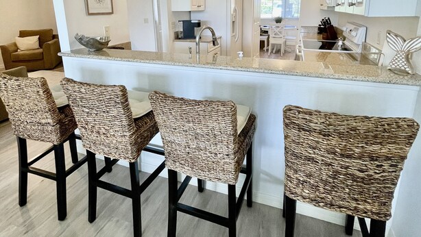 A modern kitchen with white cabinets, a central island with chairs, and a dining area with a light-colored table and chairs.