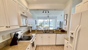 A modern kitchen with white cabinetry, a granite countertop, stainless steel appliances, and a view to the outside.