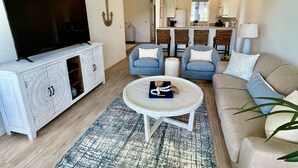 A modern living room with a flat-screen TV, a white cabinet, a round coffee table, a beige sofa, and a ceiling fan.