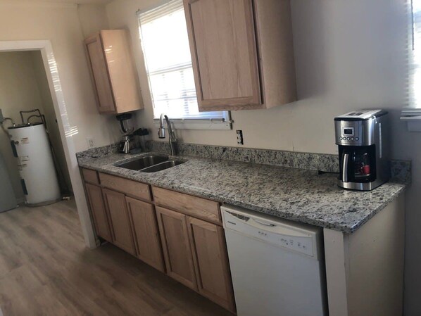 A kitchen with a granite countertop, a coffee maker, a dishwasher, and wooden cabinets.