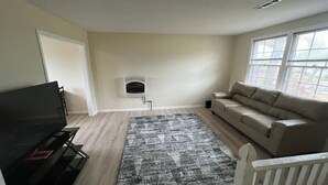 Ein Wohnzimmer mit Flachbildfernseher, einem beigefarbenen Sofa, einem gemusterten Teppich und einem Kamin.