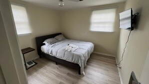 Ein Schlafzimmer mit Bett, Deckenventilator, Fernseher und einem Fenster mit Jalousien.