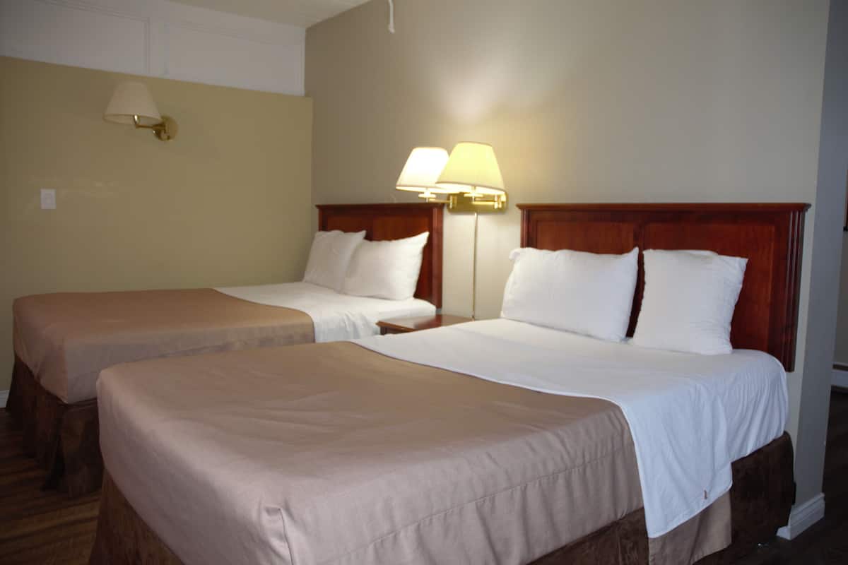 Two single beds with wooden headboards, beige bedding, and a wall-mounted lamp.