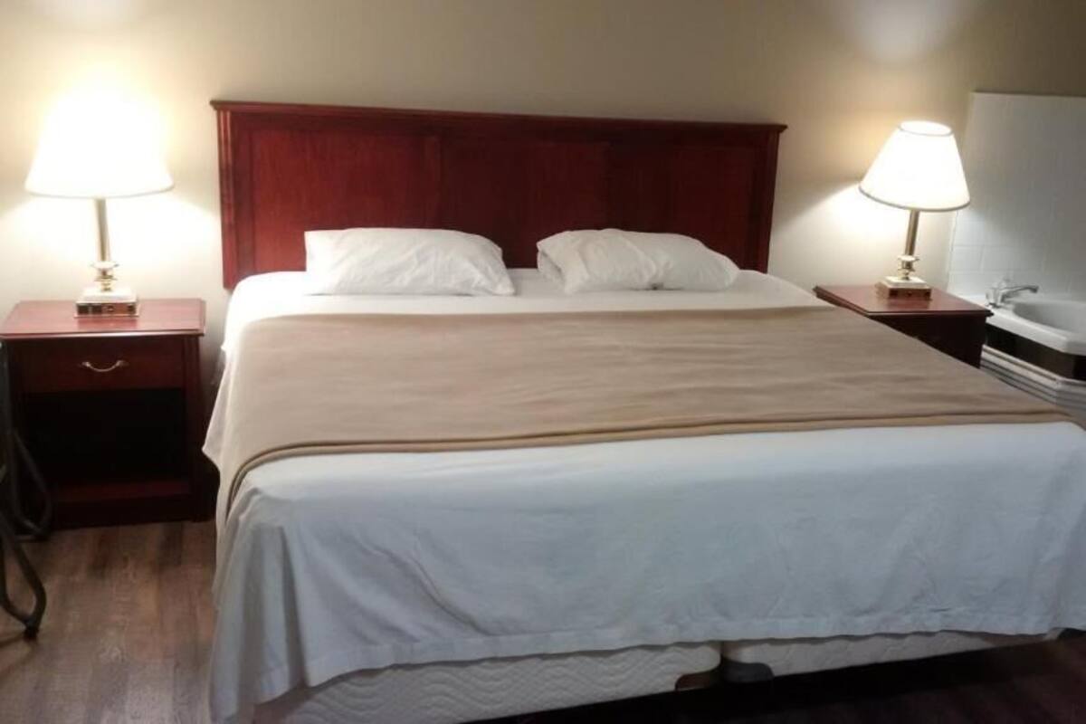 A hotel room with a large bed, two bedside tables with lamps, a wooden headboard, and a bathtub.