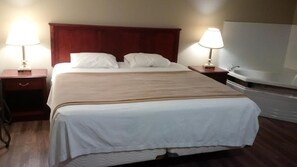 Ein Hotelzimmer mit einem großen Bett, zwei Nachttischen mit Lampen, einem Holzkopfstück und einer Badewanne.