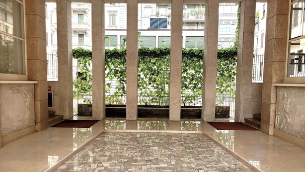 A spacious lobby with a polished floor, large columns, and a view of greenery outside.