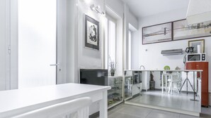 A modern kitchen with white cabinetry, a glass door leading to a balcony, and a dining area with a white table and chairs.