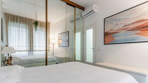 A hotel room with a large bed, a bench, a mirror, a painting, and a window with curtains.