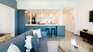 Eine moderne Küche mit Kochinsel, Barhocker und Essbereich mit Sofa und Kissen.