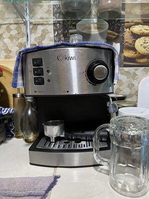 A kitchen with a stainless steel coffee maker, a glass pitcher, and a mug on the counter.