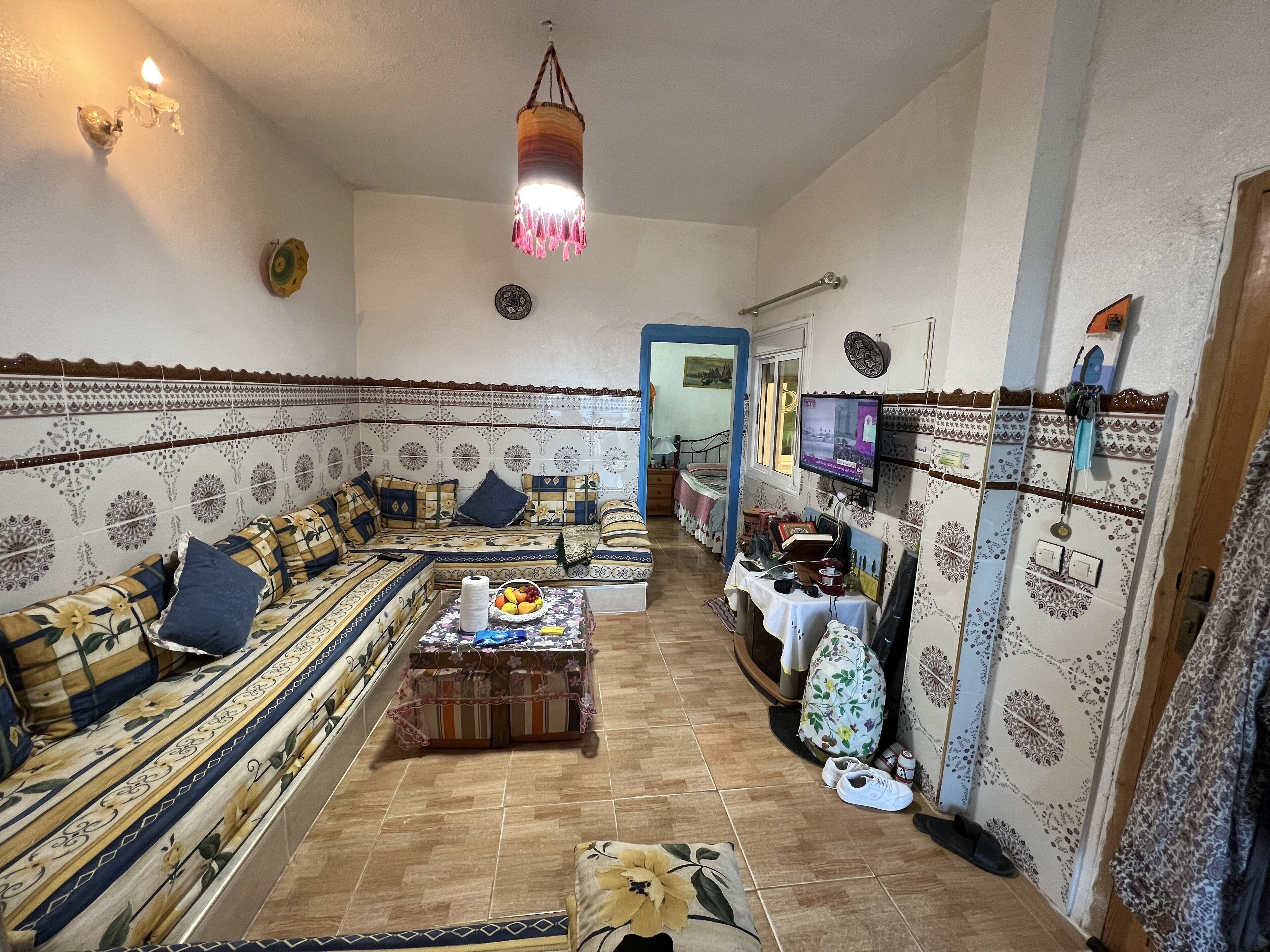 Un salon chaleureux avec des murs à motifs, un ensemble de canapés, un téléviseur et une lampe décorative suspendue.