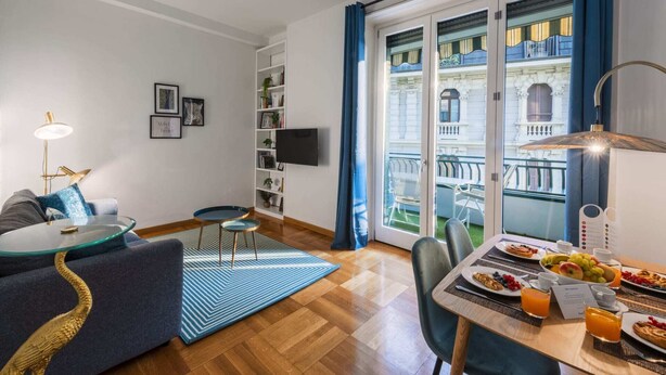 Ein modernes Wohnzimmer mit Sofa, Glastisch, Bücherregal und Essbereich mit Frühstück.