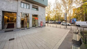 Ein modernes Gebäude mit einer Stein-Fassade, großen Fenstern und einem gut sichtbaren Eingang mit einem roten Schild.