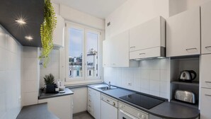 Eine moderne Küche mit weißen Schränken, einer schwarzen Arbeitsplatte, einem eingebauten Ofen und einem Fenster mit Blick auf die Stadt.