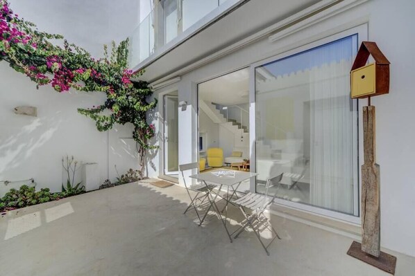 Ein modernes Haus mit Glastür, die zu einer Treppe führt, einem Essbereich mit Tisch und Stühlen sowie einem Vogelhaus an der Wand.