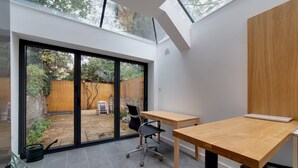 A modern interior with a large sliding glass door leading to a backyard, a wooden desk, and a black office chair. - Bright Beautiful Modern 2 Bed Home Pass The Keys (Cambridge)