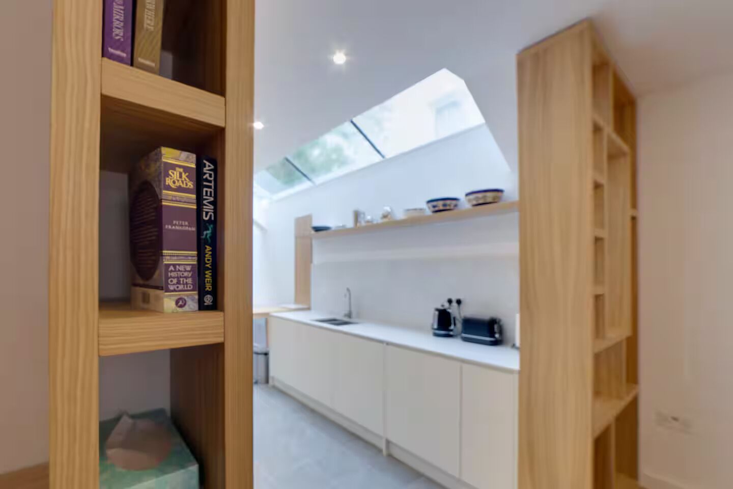 A modern kitchen with white cabinetry, a skylight, and a built-in shelf with kitchenware.