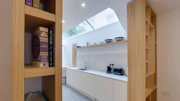 A modern kitchen with white cabinetry, a skylight, and a built-in shelf with kitchenware.