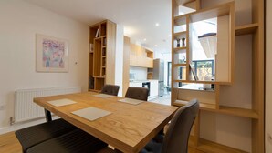 A modern kitchen with built-in appliances, a dining area with a wooden table and chairs, and a bookshelf with books. - Bright Beautiful Modern 2 Bed Home Pass The Keys (Cambridge)