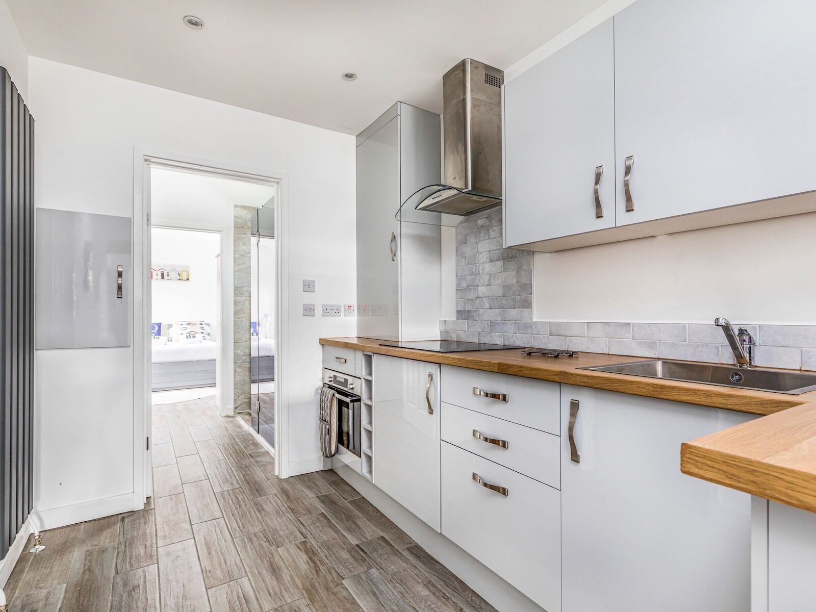 A modern kitchen with white cabinets, a stainless steel range hood, and a wooden countertop.