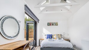 Un dormitorio con cama, escritorio, silla, espejo redondo y vistas al exterior.