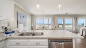 A kitchen with a granite countertop, stainless steel sink, and a dishwasher. There is a painting on the wall and a view of the balcony. - Gulf-front, private pool, pets welcome! (Port Saint Joe)