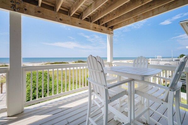 A wooden deck with white chairs and a table overlooking a beach.