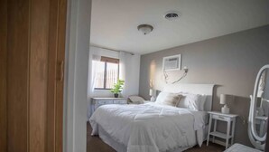 Quarto com uma cama grande, mesas de cabeceira, um criado-mudo, um espelho e uma janela com cortinas.