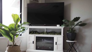Uma sala de estar com televisão de tela plana montada acima de uma lareira branca, com duas plantas em vasos de cada lado.