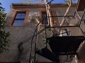 A building with two air conditioning units on the exterior wall, a window with a wooden frame, and a metal structure with plants. - Titan House Hostel (Izmir)