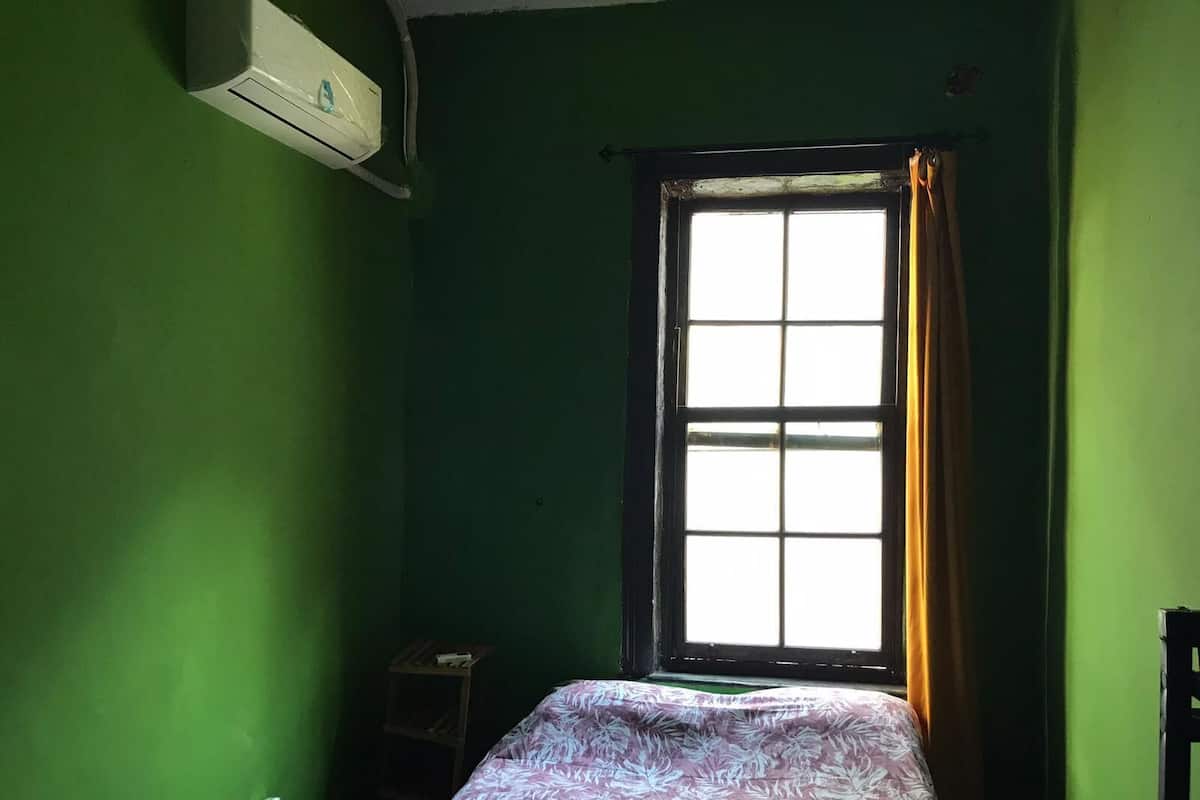 A small room with a single bed, a window with curtains, and an air conditioning unit on the wall.
