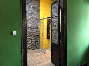 A hallway with a stone wall, a yellow door, and a black door. - Titan House Hostel (Izmir)