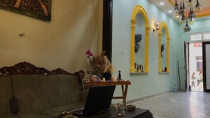 A room with a sofa, a table with a laptop, a vase with flowers, and a large window with a view of the street. - Titan House Hostel (Izmir)