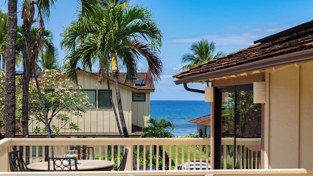 A balcony with a view of the ocean, palm trees, and a building with a tiled roof.