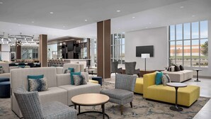 Un moderno vestíbulo de hotel con zona de estar, una cocina al fondo y grandes ventanales.