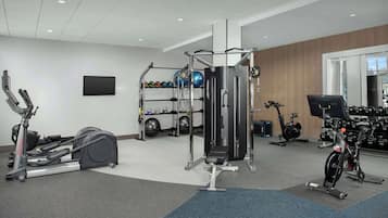 Une salle de sport équipée de machines de cardio, de matériel de musculation et d’un téléviseur fixé au mur.