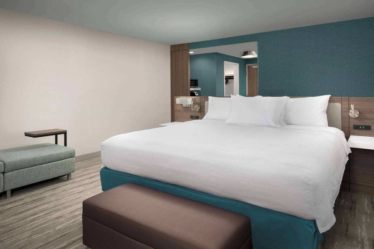 Moderni hotellihuone, jossa on suuri sänky, pieni sohva, penkki ja peili.